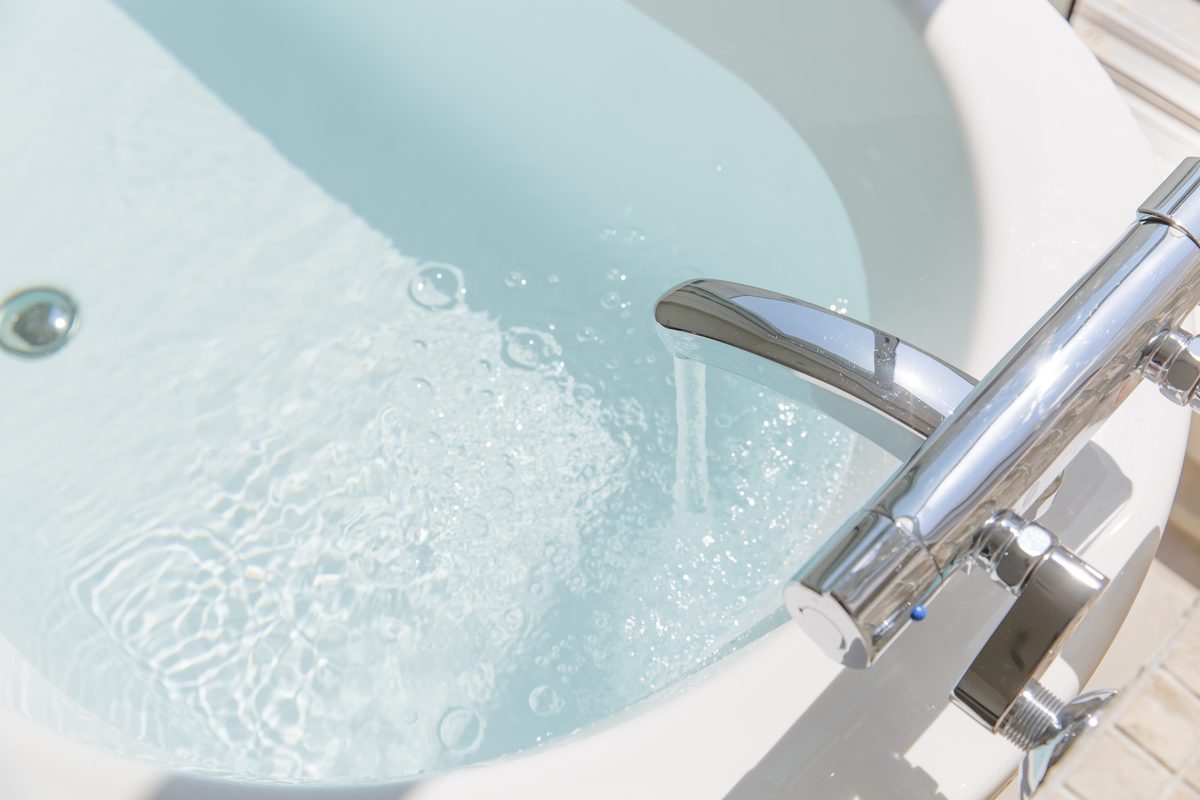 Close view of a chrome bath mixer filling a white bath with clear water