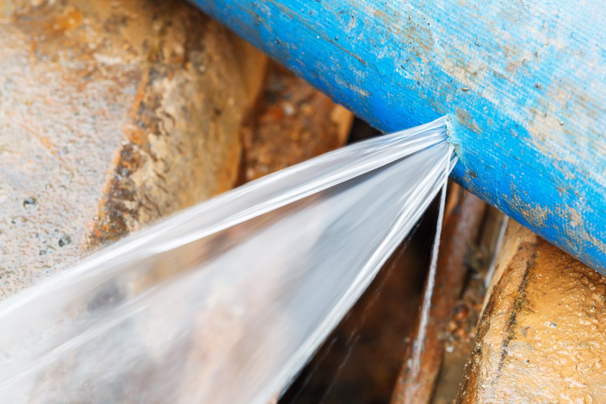 Water spraying out of a split in a blue pipe above a muddy trench