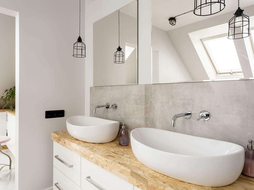 A bright bathroom with two white bowl basins on a timber vanity top, wall-mounted taps and a wide mirror